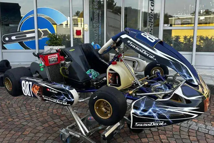 Blaues und schwarzes Go-Kart mit Blitzpfeil-Aufklebern, mit goldgeränderten Reifen und einem sichtbaren Motor.