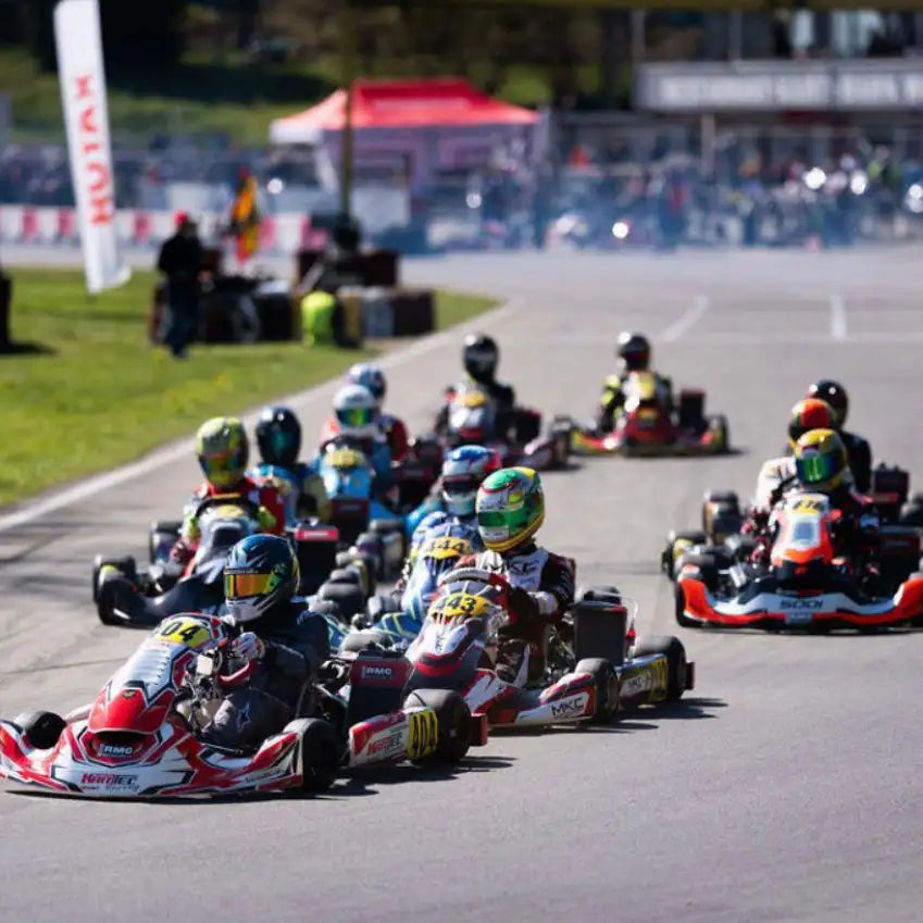 Roter und weißer Go-Kart mit schwarzen Rädern und Sponsorenaufklebern, die auf einer Strecke Rennen fährt.
