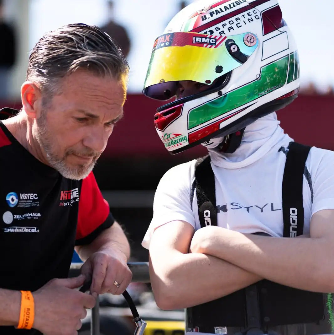 Weißer Rennhelm mit lebendigen Akzenten in Gelb, Grün und Rot, mit Sponsorenlogos wie „‚rmc”“ und „„sportec racing.”“